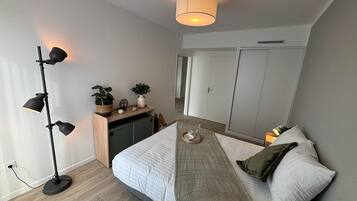 Een slaapkamer met een bed, nachtkastje, lamp, kledingkast en uitzicht op de gang.