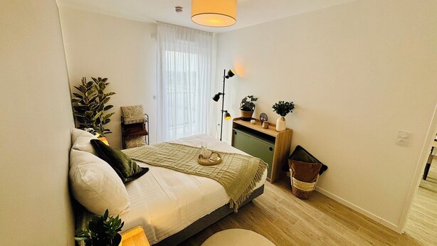 Une chambre à coucher de taille réduite, comprenant un lit, une table de chevet, une lampe et un petit coin salon.