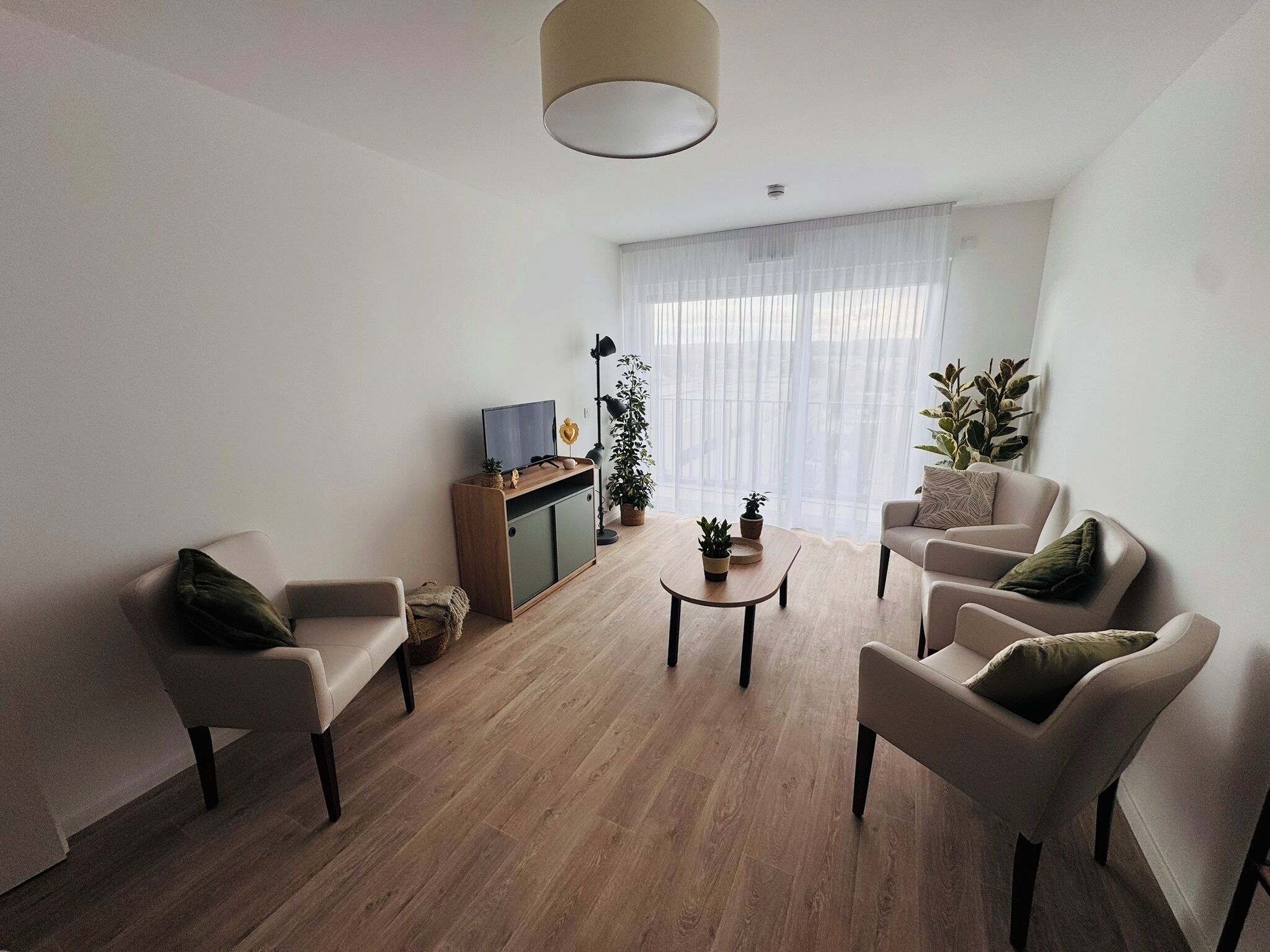 A modern living room with a wooden floor, a sofa, a coffee table, and a TV on a wooden cabinet.