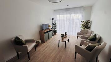 A modern living room with a wooden floor, a sofa, a coffee table, and a TV on a wooden cabinet.
