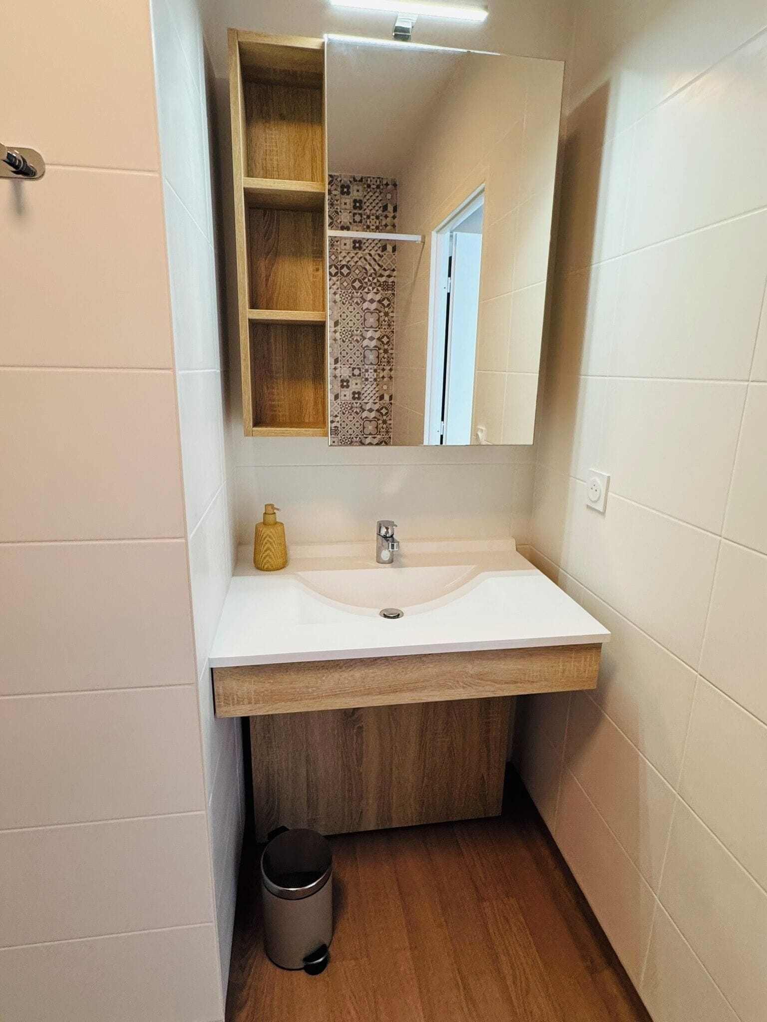 A bathroom with a white sink, wooden vanity, and a mirror.