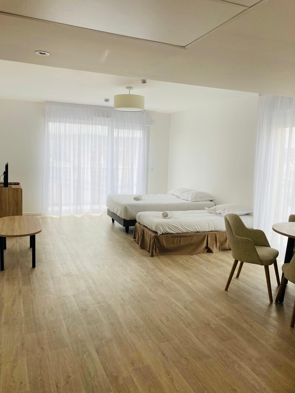Ein modernes Hotelzimmer mit einem Bett, zwei Nachttischen, einem Sessel, einem kleinen Tisch und einem Fenster mit durchsichtigen Vorhängen.
