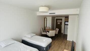 A hotel room with two beds, a desk, a chair, a TV, and a kitchenette.