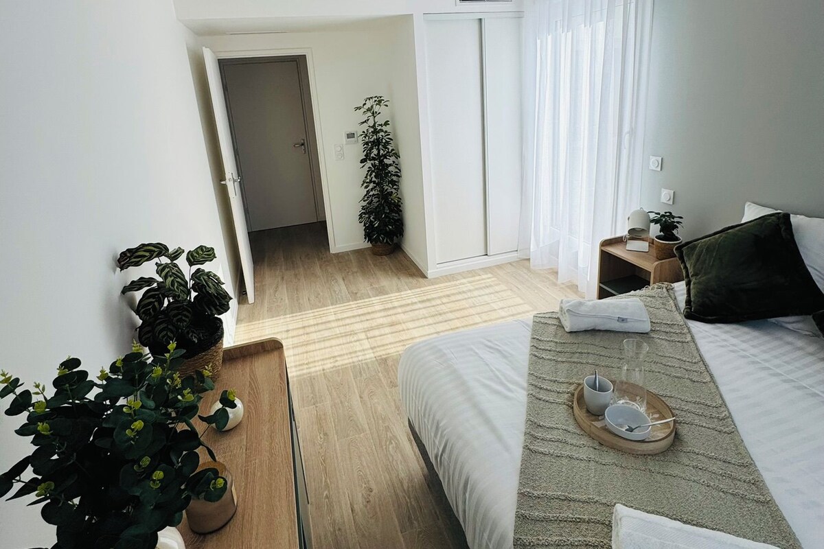 Een moderne hotelkamer met een groot bed, een nachtkastje met dienblad, een potplant en uitzicht op de gang.