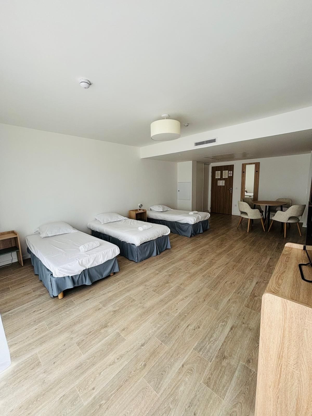 Una habitación de hotel con tres camas individuales, un escritorio de madera, una silla y una mesita.