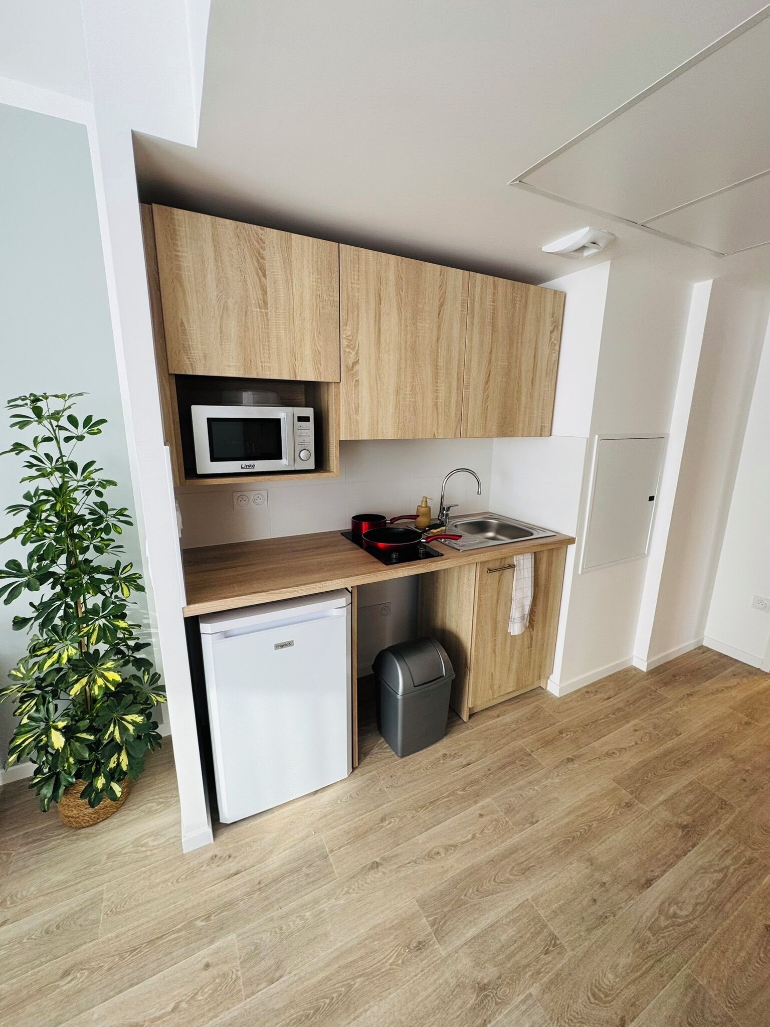 Une cuisine compacte avec des meubles en bois, un four à micro-ondes, un évier et un petit réfrigérateur.