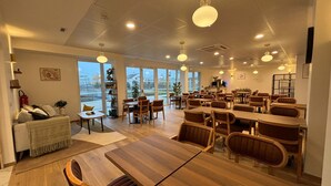 Un vaste espace dédié à la salle à manger, avec des tables et des chaises en bois, de grandes fenêtres offrant une vue sur l’extérieur et un plafond orné d’un motif ajouré.