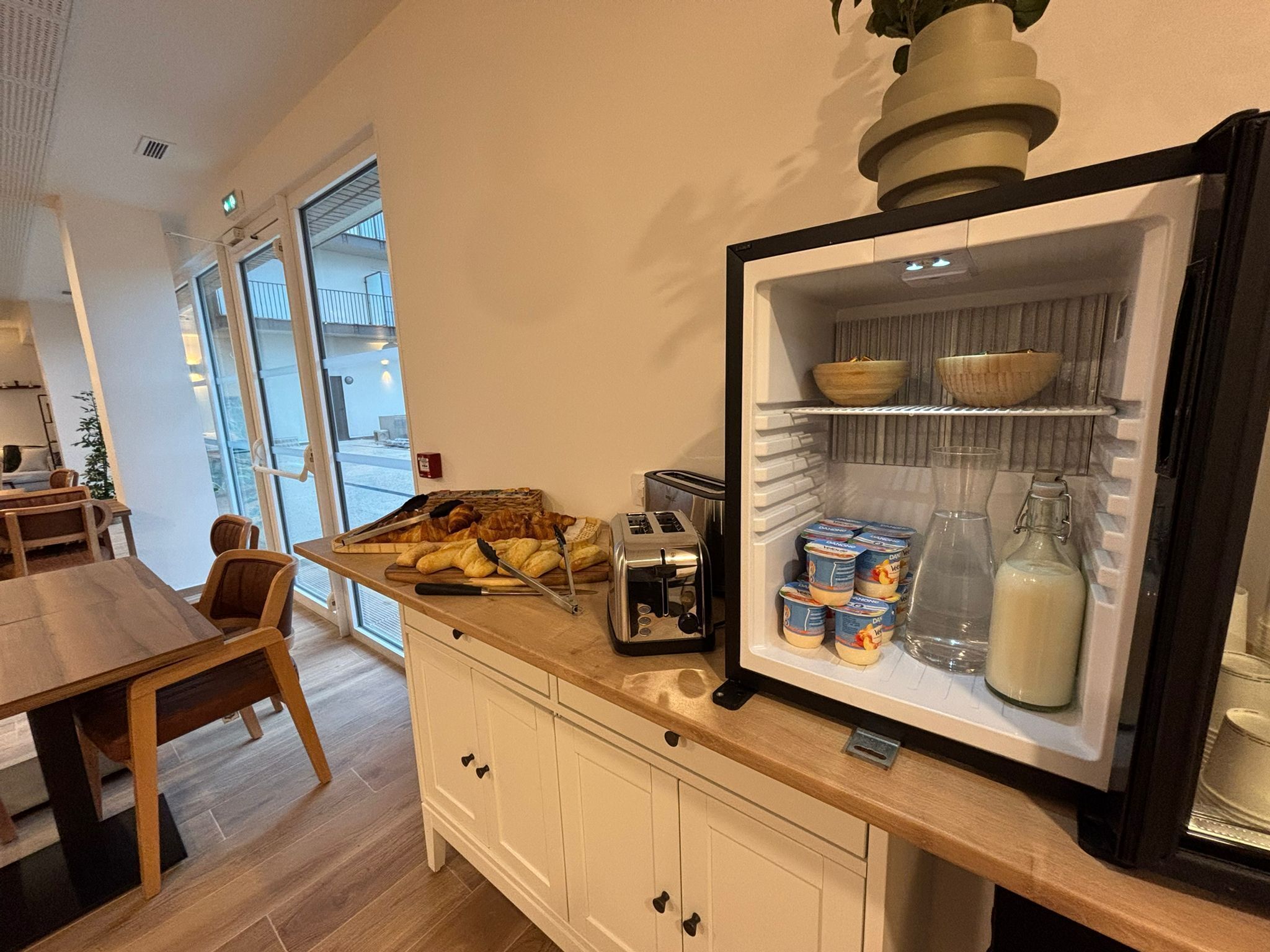 A breakfast bar with croissants, a toaster, and dairy products in a well-lit room with a view of the outside.