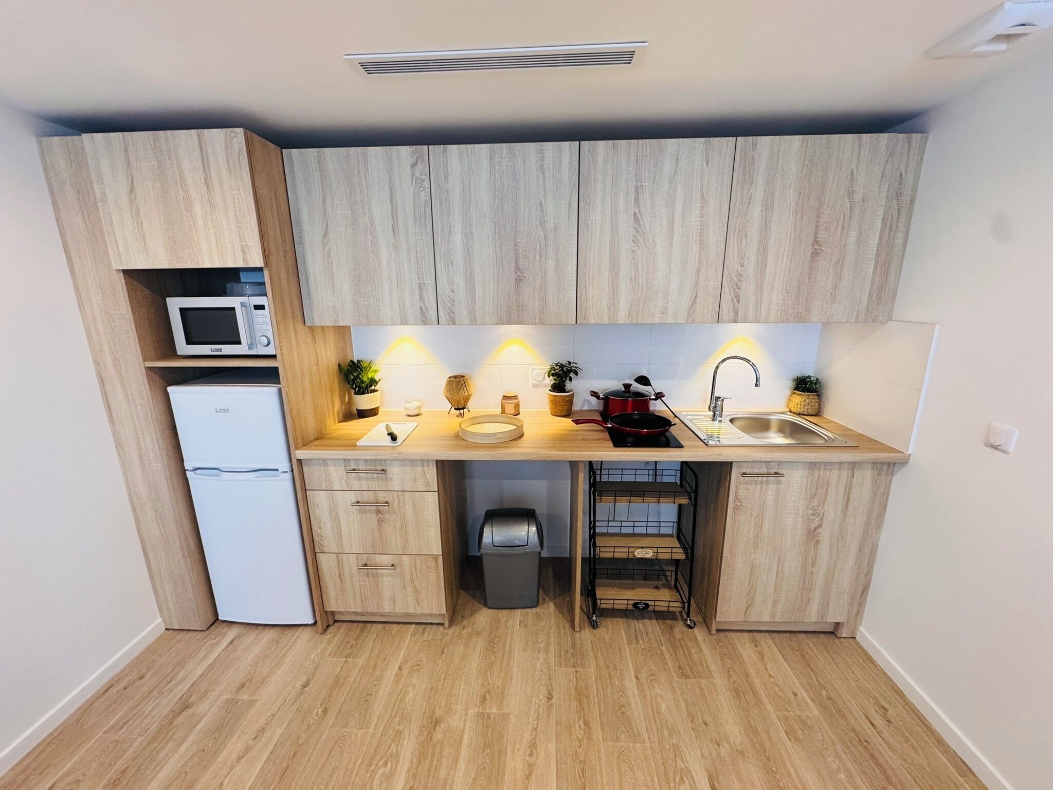 Une cuisine compacte avec des meubles en bois, un four à micro-ondes, un évier et une petite poubelle.