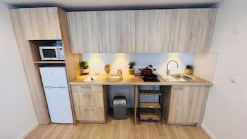 Une cuisine compacte avec des meubles en bois, un four à micro-ondes, un évier et une petite poubelle.