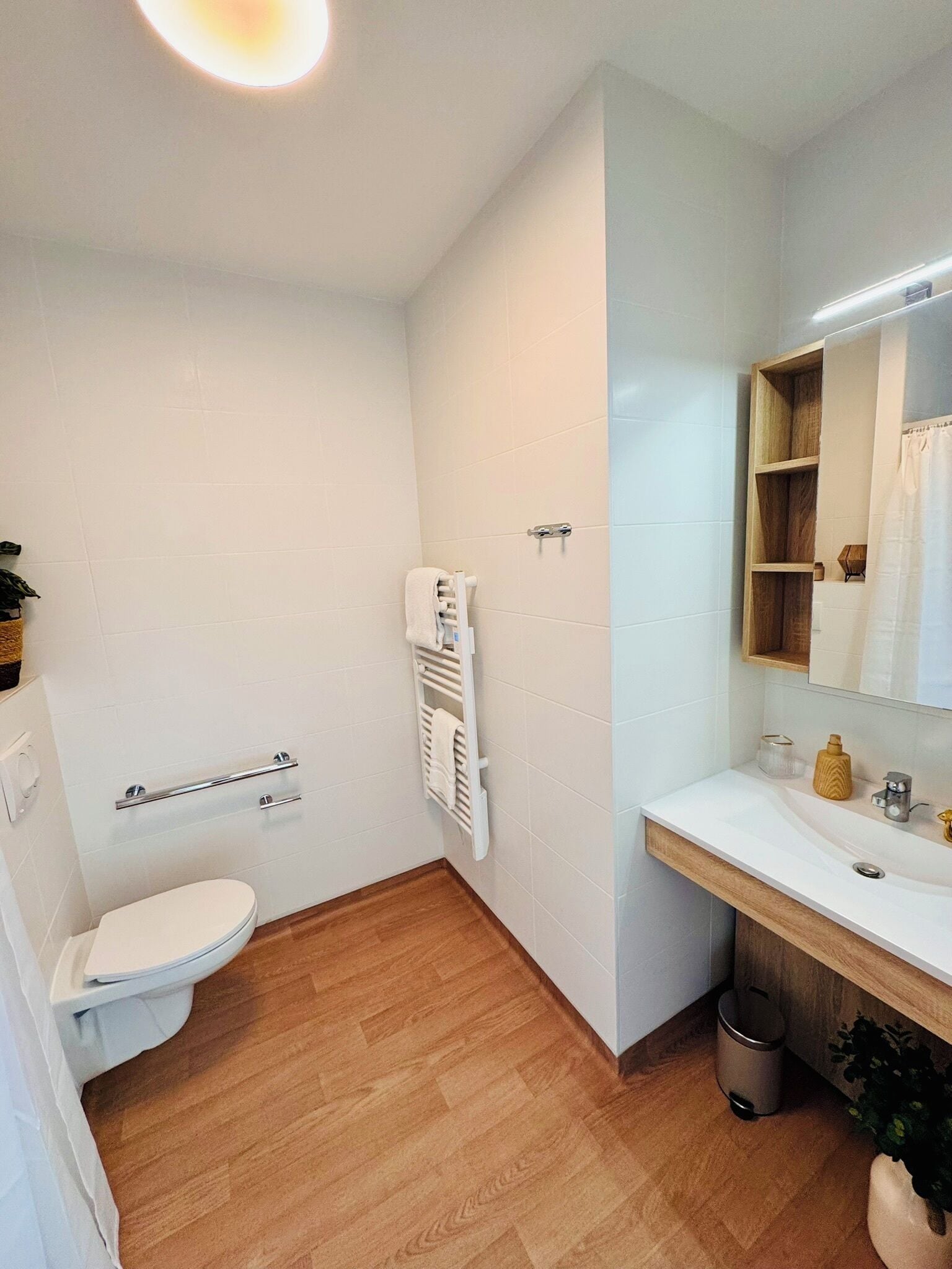 Un bagno moderno con un WC bianco, pavimento in legno, un lavandino bianco con specchio e un porta asciugamani.