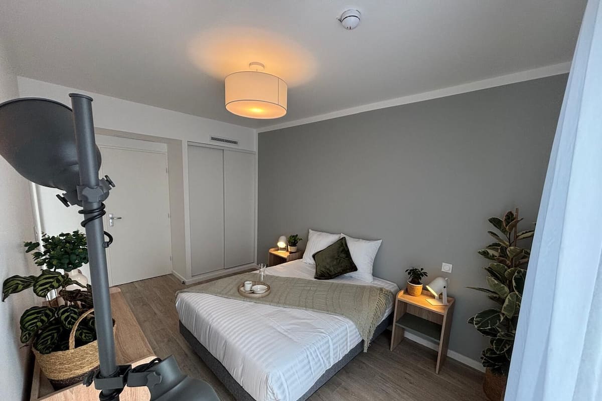 Een moderne slaapkamer met een bed, nachtkastjes, een lamp en potplanten.
