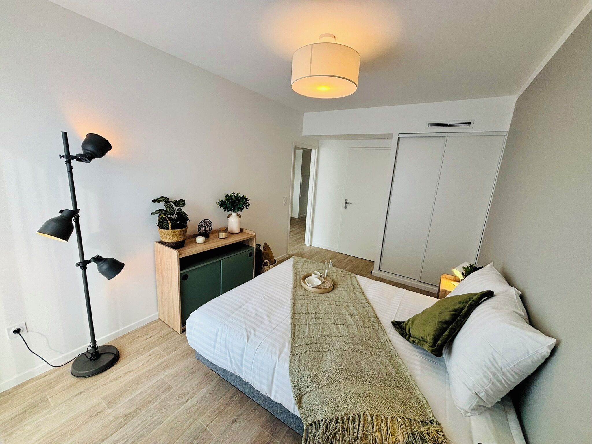 A modern bedroom with a bed, bedside table, lamp, wardrobe, and a view of the hallway.
