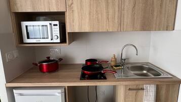 A compact kitchen with a microwave, a small fridge, a sink, and a trash bin.