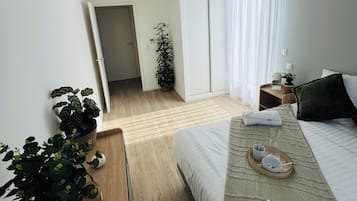 Et moderne hotelværelse med en stor seng, et natbord med bakke, en potteplante og udsigt til gangen.