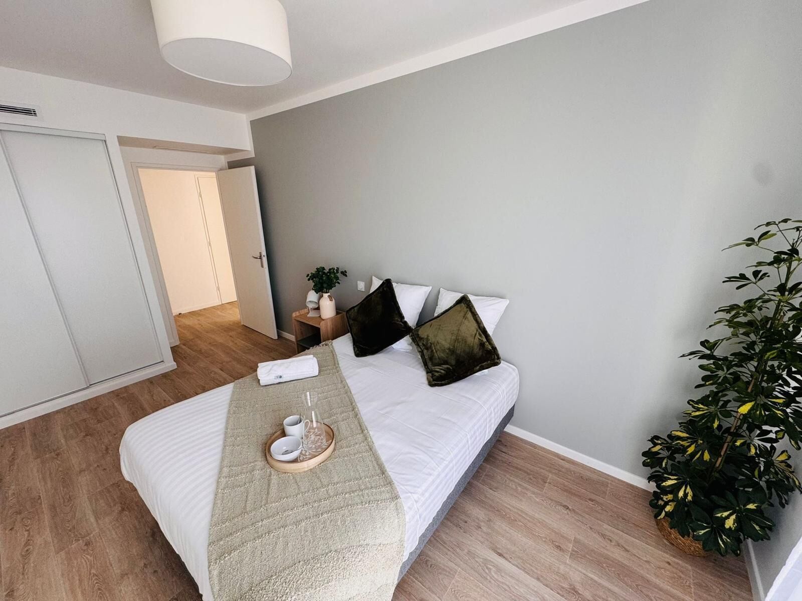 Un dormitorio con cama, mesita de noche, lámpara y planta en maceta.