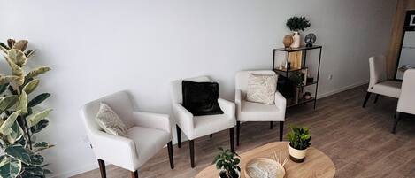 A modern living room with a wooden coffee table, white armchairs, and a potted plant.