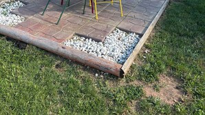 Une terrasse avec une table ronde et des chaises, un pot de fleurs et une maison en arrière-plan.