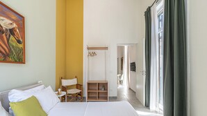 A hotel room with a bed, a chair, a small table, a shelf, and a painting on the wall. - Panurban Apartments by Wonderful Italy (Palermo)