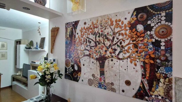 Ein Wohnzimmer mit einem großen abstrakten Gemälde an der Wand, einem Holztisch mit Blumen in einer Vase und einem Fernseher auf einem Schrank.
