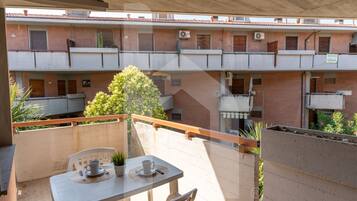 Un balcone con tavolo e sedie, una pianta in vaso e vista su un edificio a più piani con balconi e condizionatori.