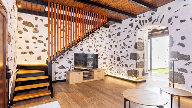 A modern interior with a wooden staircase, a TV on a wooden cabinet, and a stone wall.