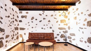 A room with a brown leather sofa, two round wooden tables, and a stone wall.
