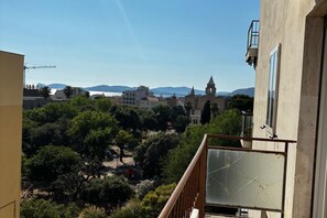 Un balcón con vistas a un pueblo, árboles y montañas a lo lejos.