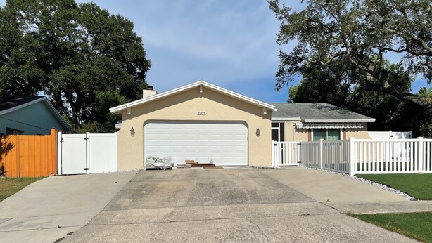 A residential garage with a beige exterior, white garage door, and a white picket fence. - Charming studio & kitchenette in wonderful Palm Harbor with AC & laundry access (Palm Harbor)