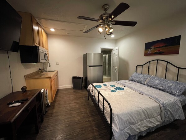 Ein Schlafzimmer mit Bett, Deckenventilator, Kühlschrank, Mikrowelle und kleinem Schreibtisch.