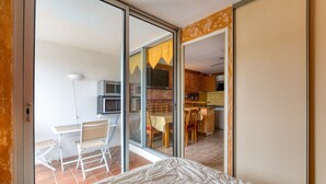 A room with a bed, a sliding glass door leading to a dining area, and a kitchenette.