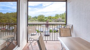 A balcony with a table and chairs, a view of a parking lot, and trees in the background.