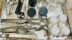 A drawer with various kitchen utensils and containers, including spoons, knives, and jars.