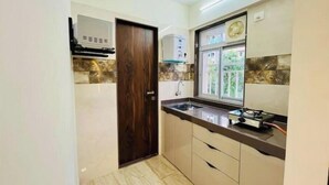 A compact kitchen with a dark wooden door, a window with a view, and a ceiling fan.