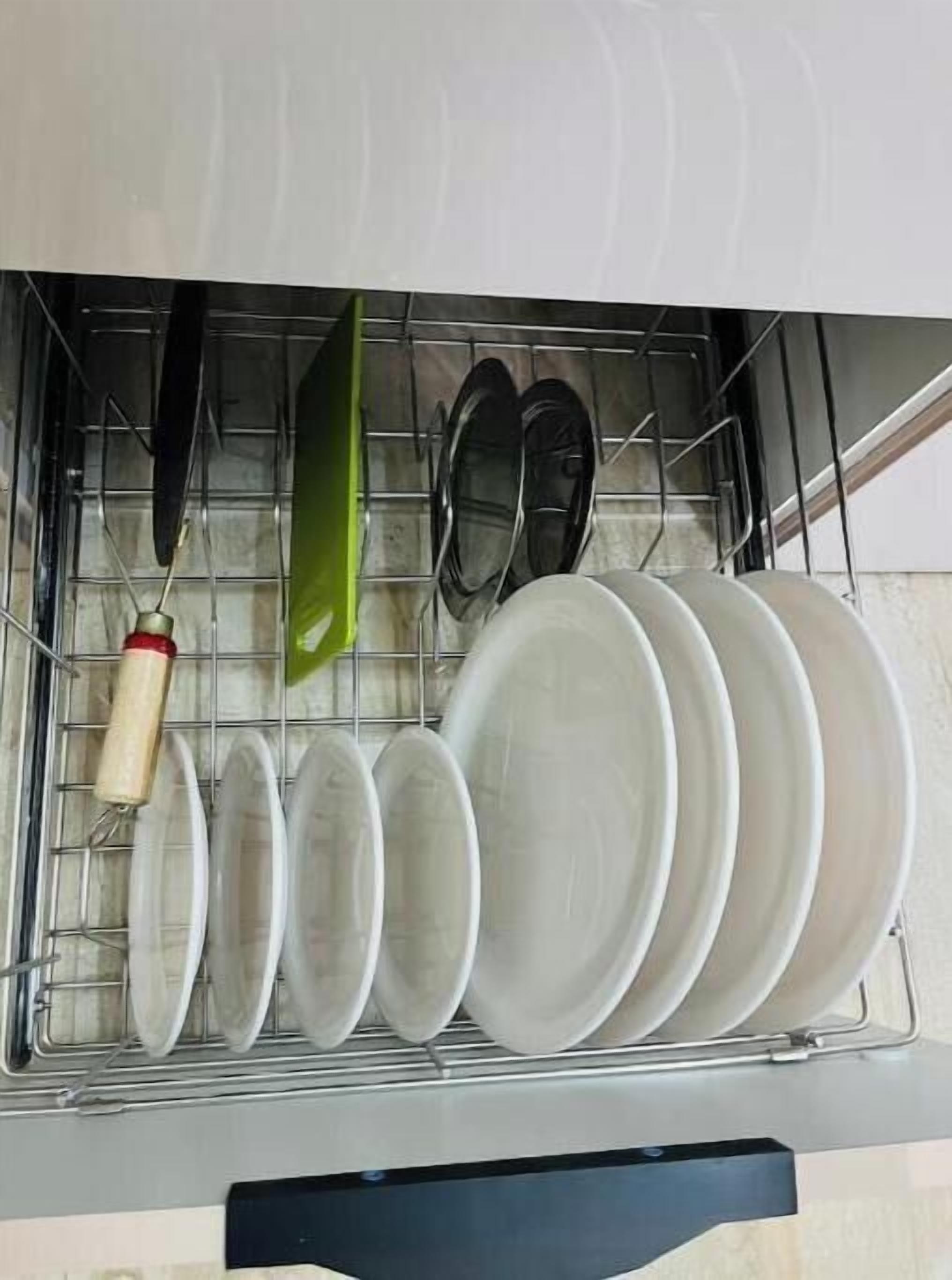A dishwasher with various dishes and utensils inside, including plates, bowls, and a green spatula.