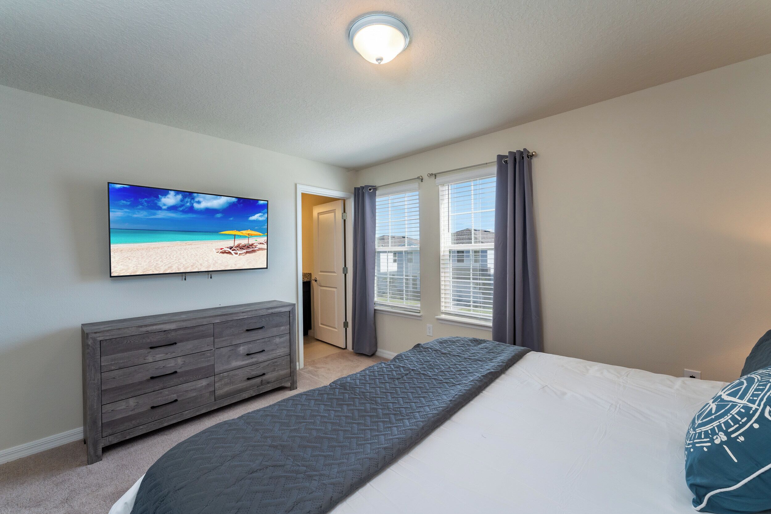 A bedroom with a bed, a dresser, a TV on the wall, and a window with curtains.