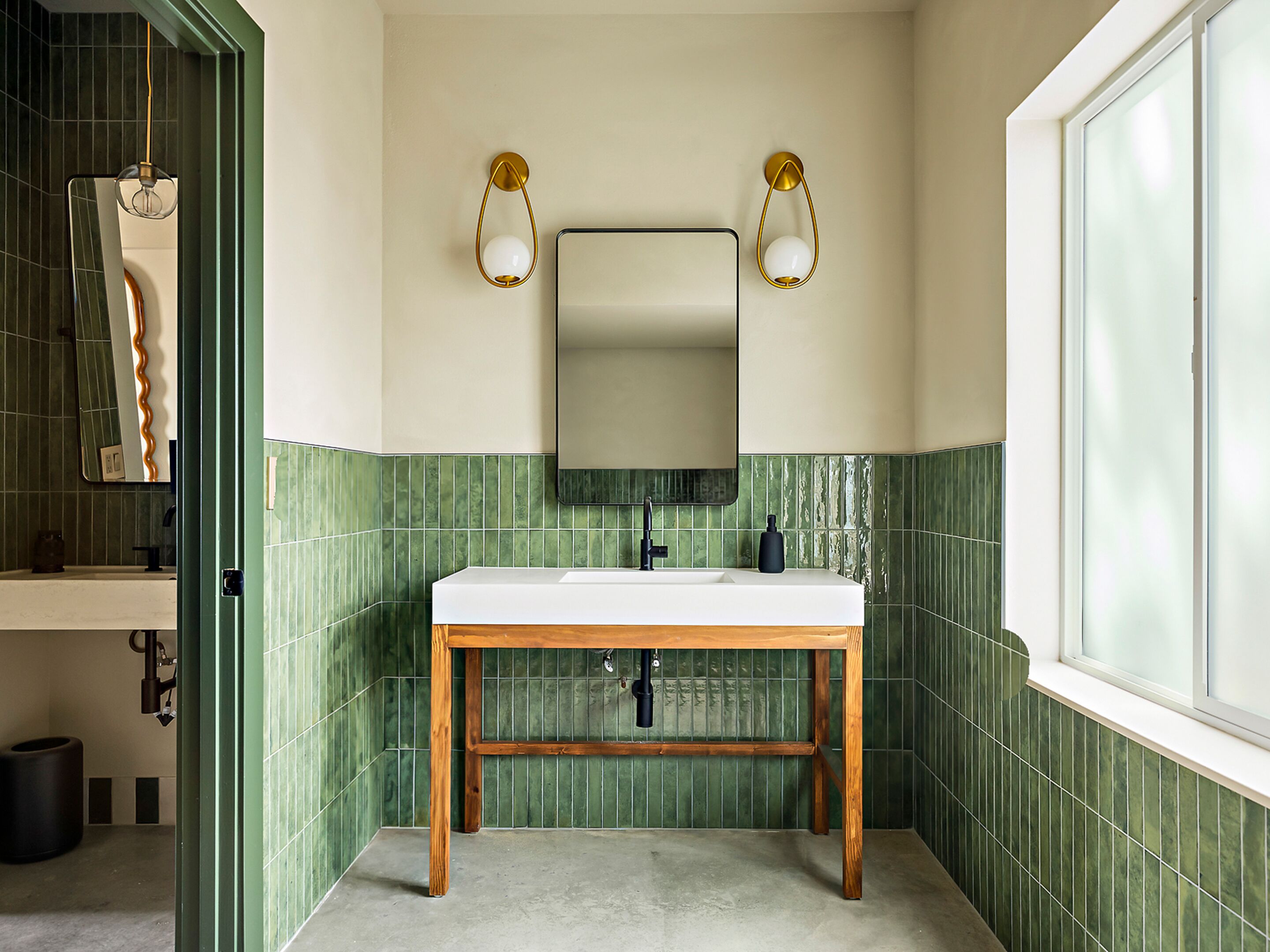 A bathroom with a white sink, green tiled walls, and a mirror with gold fixtures.
