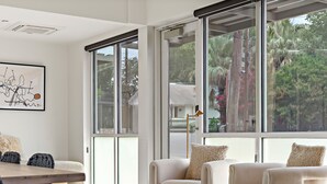Un salon moderne doté de grandes portes-fenêtres coulissantes, d’un design minimaliste et offrant une vue sur la verdure environnante.