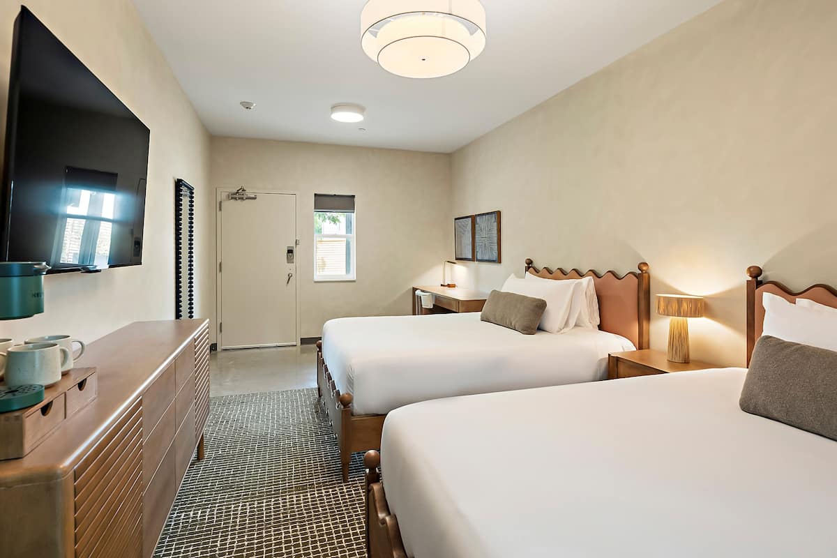 A hotel room with two beds, a television, a desk, and a window.