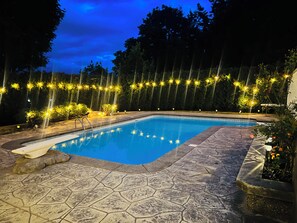 A swimming pool with a stone deck, surrounded by trees and string lights. - Rent-A-Vibe (Abbotsford)