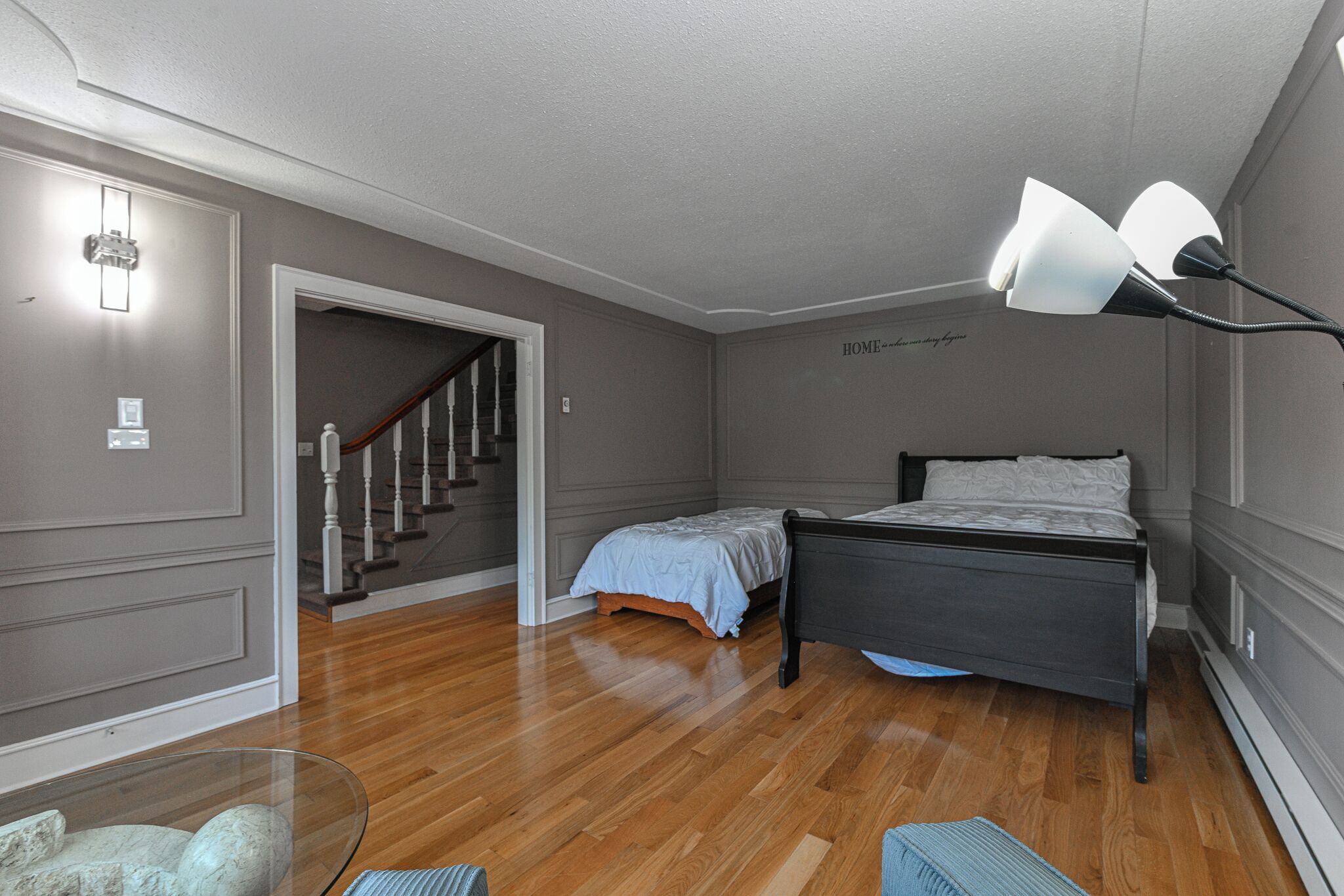 A bedroom with a bed, a nightstand, a glass table with decorative items, and a staircase leading to another room.