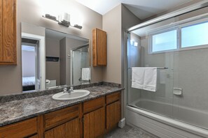A modern bathroom with a granite countertop sink, wooden cabinets, a large mirror, and a glass-enclosed shower. - Rent-A-Vibe (Abbotsford)