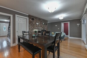 A dining area with a wooden table and chairs, a stone accent wall, and a red door in the background. - Rent-A-Vibe (Abbotsford)