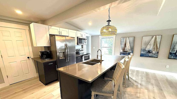 A modern kitchen with a central island, stainless steel appliances, and a chandelier. - Beautiful Lakehouse close to everything! (Huron)