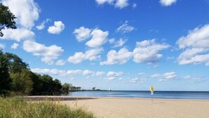 A beach with a clear sky, a lighthouse in the distance, and a lifeguard sign. - Beautiful Lakehouse close to everything! (Huron)