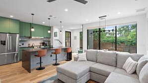 Une cuisine moderne avec des meubles de couleur verte, un réfrigérateur en acier inoxydable et un coin bar avec des tabourets.