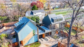 Une maison moderne avec un toit bleu, une grande terrasse et un jardin.