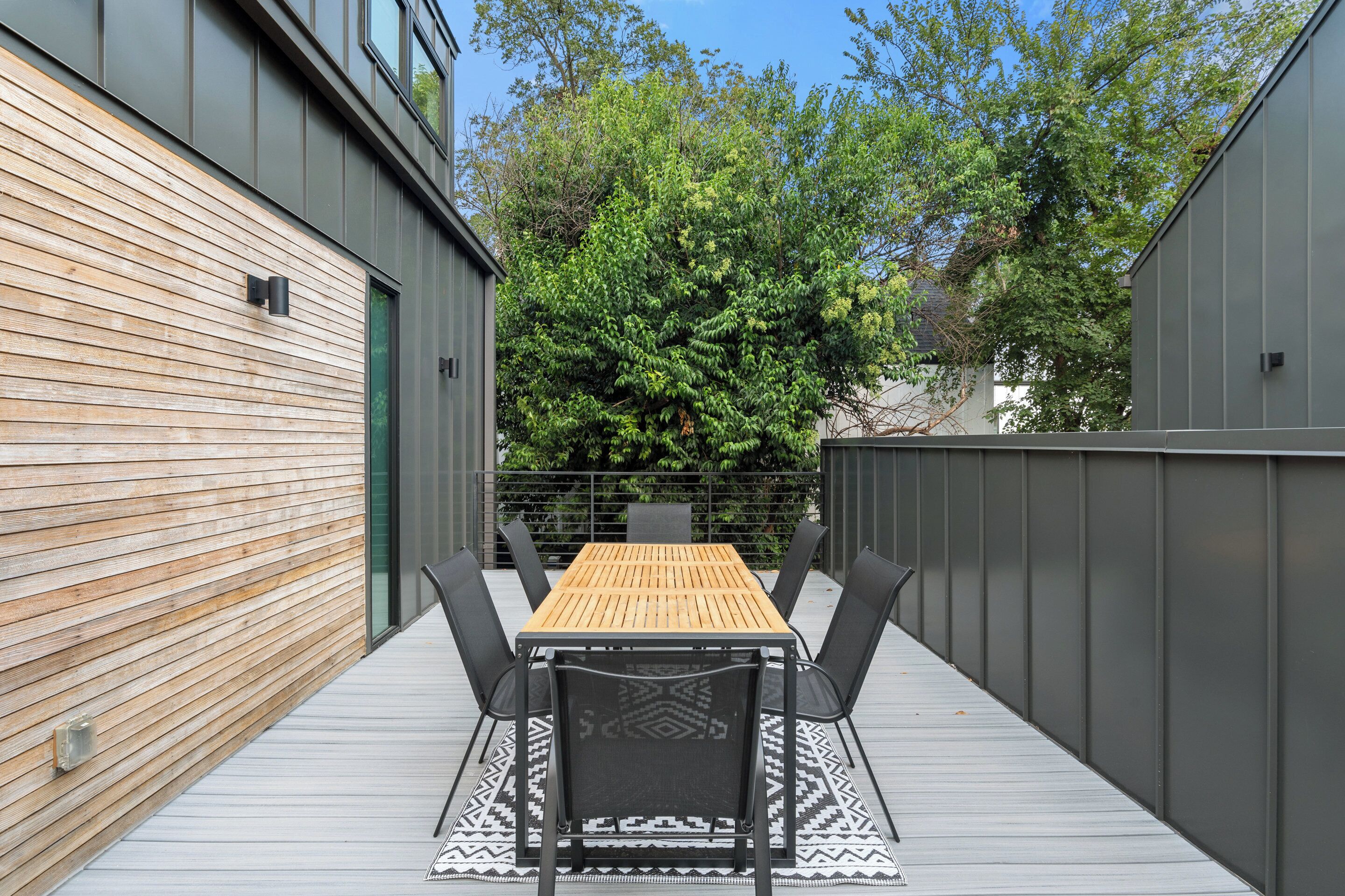 An outdoor patio with a wooden table and chairs, surrounded by metal walls and a wooden deck.