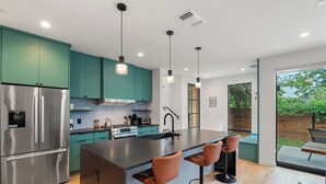 Une cuisine moderne avec des armoires de couleur turquoise, des appareils en acier inoxydable, un îlot central doté de tabourets de bar et une vue sur l’extérieur.