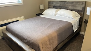 Een slaapkamer met een houten bedframe, een grijze spreidek en een nachtkastje met een lamp.